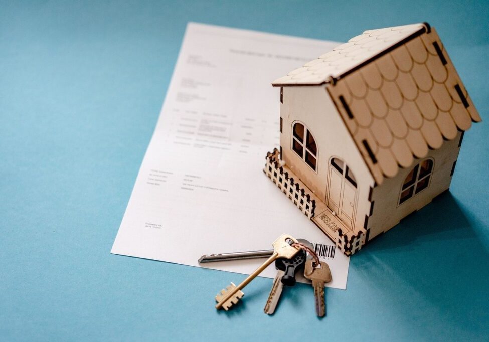 Miniature house, keys, and document on table.